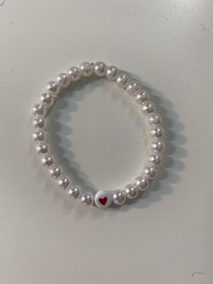 a bracelet with white pearls and a red heart on the clasp is sitting on a table