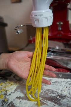 a person is holding noodles in front of a blender with the pasta coming out