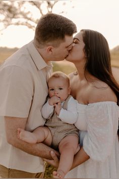 a man and woman holding a baby in their arms while they are kissing each other