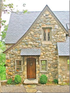 a stone house with a wooden door and window on the front porch is surrounded by greenery