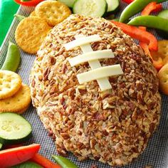 a football ball covered in cheese surrounded by crackers and veggies