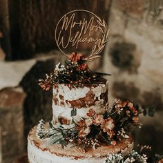 a three tiered wedding cake with flowers and greenery on the top is decorated with mr and mrs handwritten