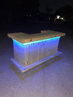 a wooden bar with blue lights on it in the middle of a parking lot at night