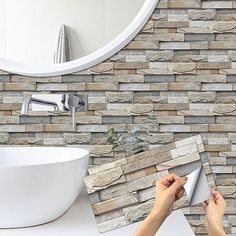 a person holding a mirror in front of a bathroom wall with stone tiles on it