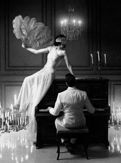 a woman in a white dress is sitting at a piano with a man standing next to her