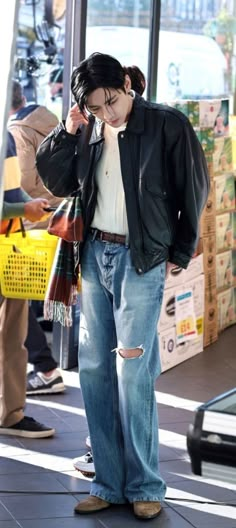 a man standing in front of a store talking on a cell phone while wearing ripped jeans and a leather jacket