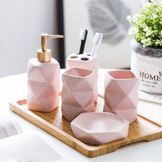 pink bathroom accessories sitting on top of a wooden tray next to a potted plant