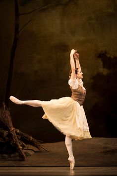 the ballerina is wearing a white dress and has her arms in the air as she balances on one leg