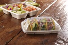 three plastic containers filled with food on top of a wooden table next to another container