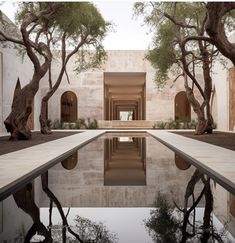 an empty pool surrounded by trees in front of a white building with a reflection on the water