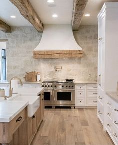 a large kitchen with white cabinets and wood flooring, along with a stainless steel range hood