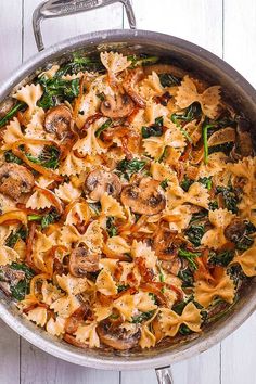 a pan filled with pasta and mushrooms on top of a white wooden table next to a knife