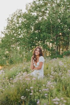 a woman is standing in the middle of a field with flowers and trees behind her