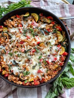 a skillet filled with meat and vegetables on top of a striped table cloth next to silverware