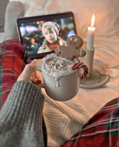 a person holding a cup with a drink in front of a laptop on a bed