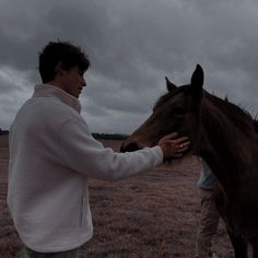 two people petting a horse on the nose in an open field with dark clouds