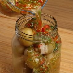 a person pouring dressing into a jar filled with potatoes and vegetables on a wooden table