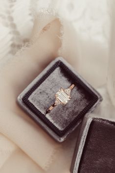 an engagement ring sitting in a velvet box on top of a white cloth covered table