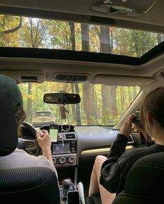 two people sitting in the driver's seat of a car looking at their cell phones