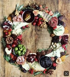 a wreath made out of cheese, fruit and nuts on a wooden table with other food items