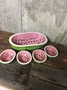 five pink and green ceramic bowls with holes in them sitting on a wooden table next to a gray wall