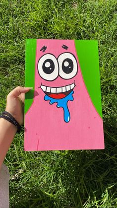 someone holding up a piece of paper with a cartoon character painted on it in the grass