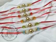 three red, white and gold beaded necklaces on a white cloth with a monogram in the middle