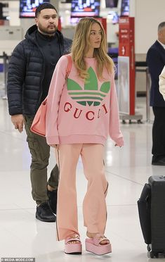 a woman in pink sweatshirt and sweatpants at an airport with her luggage behind her