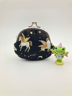 a small purse with unicorns and stars on it next to a little toy frog