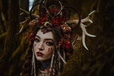 a woman with long dreads and red flowers on her head is surrounded by deer antlers