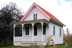 a white house with a red roof in the middle of some grass and trees behind it