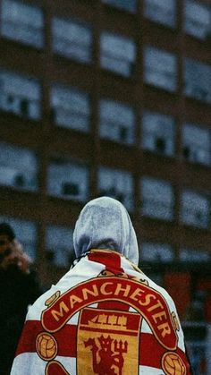 the back of a man wearing a jacket with an english crest on it, standing in front of a tall building