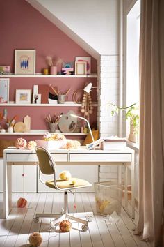 a white desk and chair in a small room with pink walls, shelves and pictures on the wall