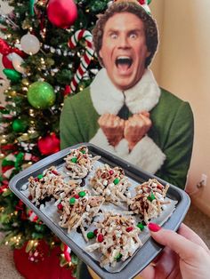 a person holding a tray with food on it in front of a christmas tree and a photo of an elf