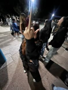 a group of people standing around each other on a street corner at night with their arms in the air