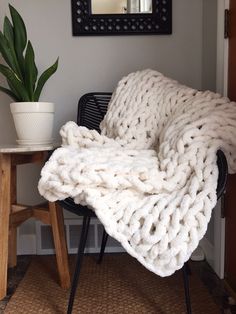 a white blanket sitting on top of a chair next to a potted plant