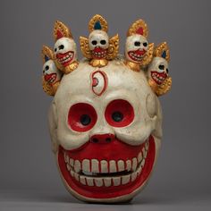 a red and white mask with five skulls on it's head, in front of a gray background