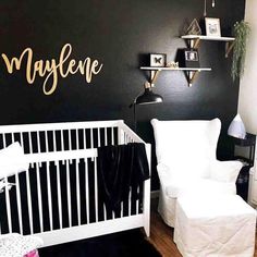 a baby's room with black walls, white furniture and gold lettering on the wall