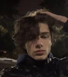 a young man with curly hair sitting in the back seat of a car at night