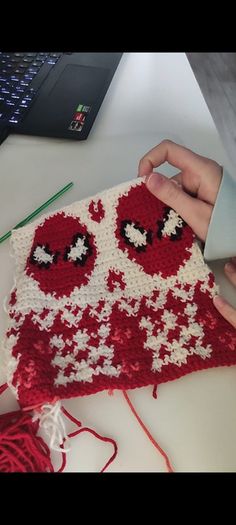 someone crocheting an ugly red and white piece of cloth with eyes on it