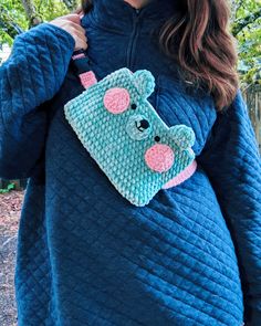 a woman is wearing a blue sweater with a crocheted bear on the pocket