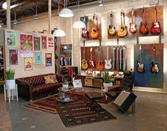 a room filled with lots of guitars hanging from the ceiling and furniture in front of them