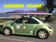 a green car with flowers painted on the side and a surfboard in the back