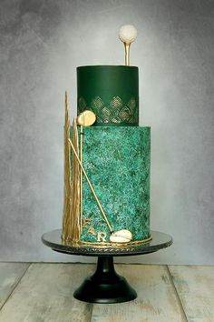 a green and gold decorated cake on a black stand with two golf tees in the middle