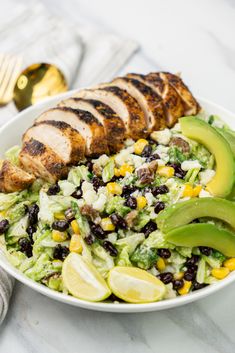 a salad with chicken, avocado and black beans in a white bowl on a marble table