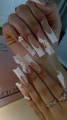 “Serenity” (Inspo Nails) •Gorgeous French Tip Nails with Sparkling White Glitter Detail, Natural Ombre Detail, Champagne Crystals & 3D Acrylic Flowers •You will receive a set of 10 nails, nail file, nail glue, wooden cuticle pusher, alcohol wipe, and detailed instructions on how to apply and remove your nail set •Please order a sizing Kit first if you do not know which size nail set to order TikTok: @Pressedbystepht Instagram: @Pressed_by_Steph_T White Nails Inspo Long Coffin, White Nail Inspo Acrylic Coffin, Wedding Nails Long Coffin, 15 Nails Ideas White, Long Square Acrylic Nails 3d Flowers, White Square Acrylic Nails With Design, Quince Nails White, Nails Acrylic With Diamonds, Clear Acrylic Nails With Rhinestones