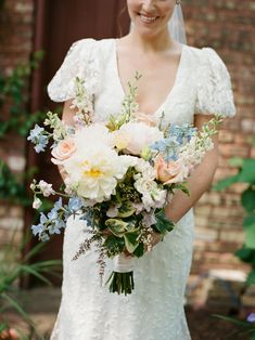 a woman in a wedding dress holding a bouquet of flowers and smiling at the camera