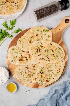 tortillas on a cutting board with herbs and seasoning next to it, surrounded by other ingredients