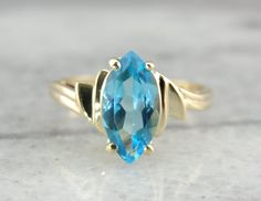 "Classic and stately, this ring is constructed of 14 karat yellow gold, and features a gorgeous richly blue Topaz in the center surrounded by sweeping shoulders of polished gold. Material: 14 Karat Yellow Gold Gem: Blue Topaz 2.08 Carats Size of Ring: 7.25 Marks: \"14K\" Stamped on inside band SKU#: Y4K6CP-D Each piece has been identified and graded by a Graduate Gemologist who has been certified by the Gemological Institute of America (GIA). We have four brick and mortar storefronts in Maine, M Gold Topaz Ring, Topaz Engagement Ring, London Blue Topaz, Marquise Cut, London Blue, Rings For Her, Topaz Ring, Cocktail Ring, Eternity Bands