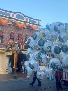 some people are walking down the street with many balloons in front of a storefront